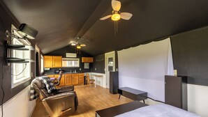 A compact room with a bed, a leather sofa, a dining table, and a kitchen area.
