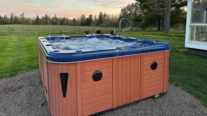 A hot tub in an outdoor setting with a grassy field and trees in the background.
