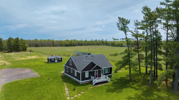 A large house with a porch and a smaller building nearby, surrounded by a grassy field and trees.