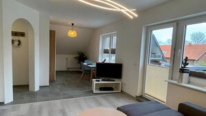 Una sala de estar moderna con un sofá, dos mesitas, un televisor y un área de comedor al fondo.