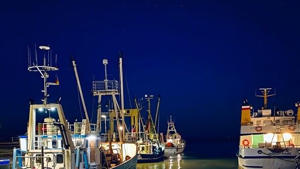 Un puerto deportivo de noche con varias embarcaciones amarradas, incluyendo una llamada 'MADONNA' y otra 'NORSTRAND'.