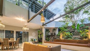 A modern outdoor living area with a dining set, wicker sofa, and a hanging light fixture. - 6 Bedroom Oasis in Burleigh Heads (Burleigh Heads)