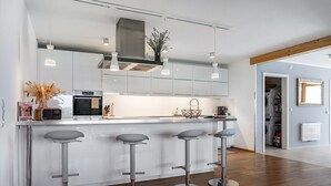 Eine moderne Küche mit Kochinsel, Barhocker, Edelstahlgeräten, Pendelleuchten und einem sichtbaren Waschbereich.