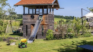 Ein hölzernes Spielhaus mit Rutsche, umgeben von einem grünen Rasen und Bäumen.