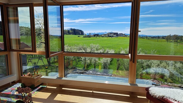 Una habitación con ventanas amplias, piso de madera, sofá rojo y una pequeña mesa con una planta.