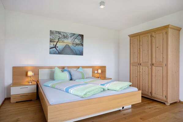 Un dormitorio con una cama de madera, mesitas de noche con lámparas, un amplio armario y un cuadro en la pared.