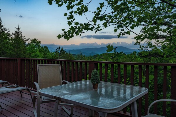 A deck with a glass table and chairs, overlooking a mountainous landscape.