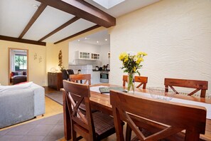 A dining area with wooden chairs and a table, a kitchen in the background, and a sofa in the foreground.