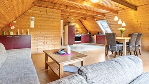 Une pièce agréable, aménagée dans un style loft, avec un plafond en bois, un coin repas doté de chaises en osier et une cuisine aux meubles rouges.