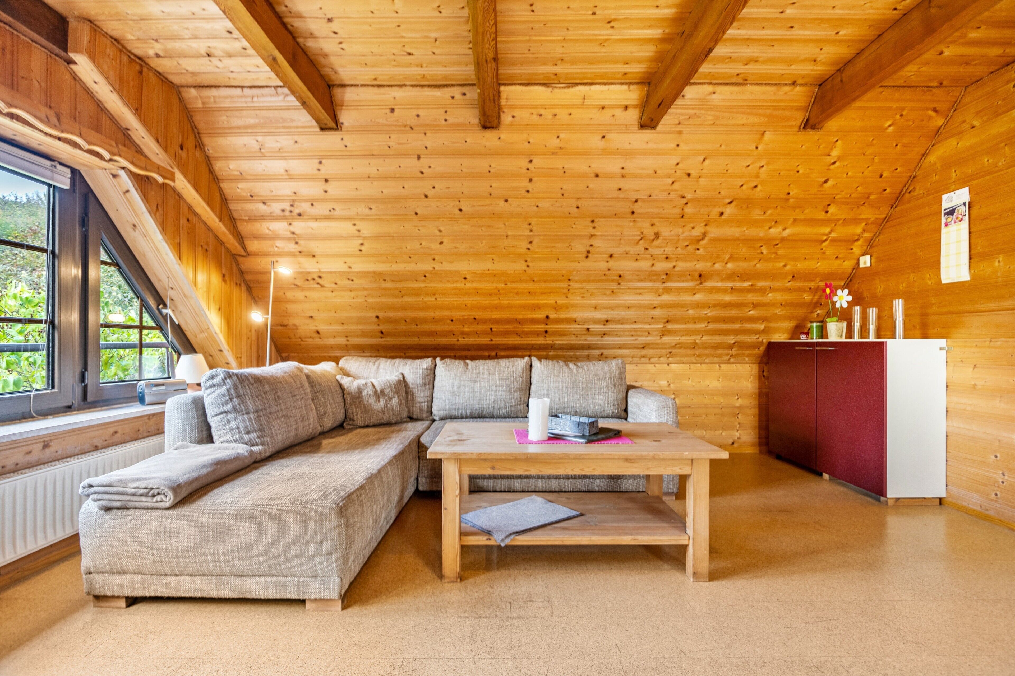 A cozy cabin with a wooden interior, a sofa, a table, and a refrigerator.