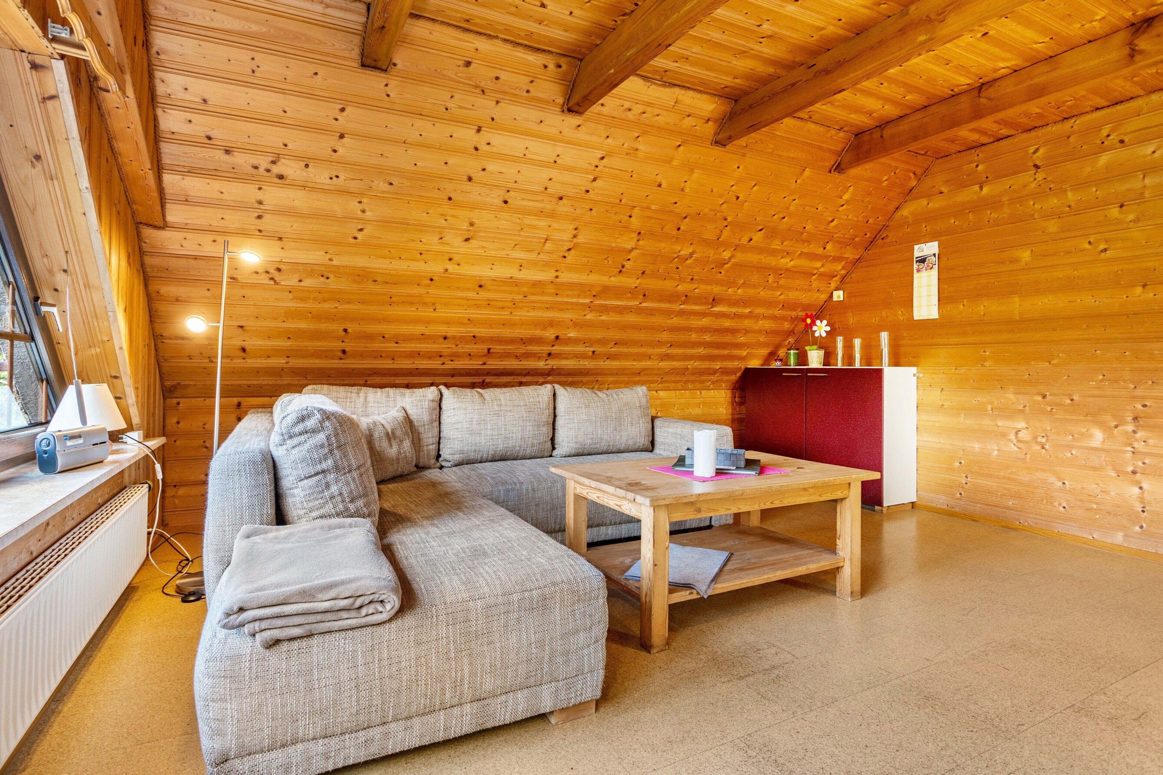 Habitació acollidora amb sostre de fusta, un sofà modular, una taula petita i un armari vermell.