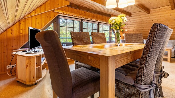 Un intérieur en bois comprenant une table à manger, des chaises, un bureau et une fenêtre donnant sur un paysage agréable.