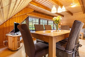 A wooden interior with a dining table, chairs, a computer desk, and a window with a view. - Apartment 'Kummerower See, 80qm' with Shared Terrace, Shared Garden and Wi-Fi (Malchin)