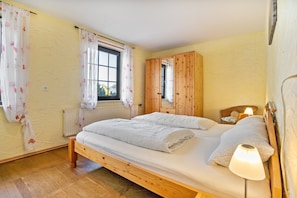 A single bed with a wooden frame, a bedside lamp, a window with curtains, and a wardrobe.