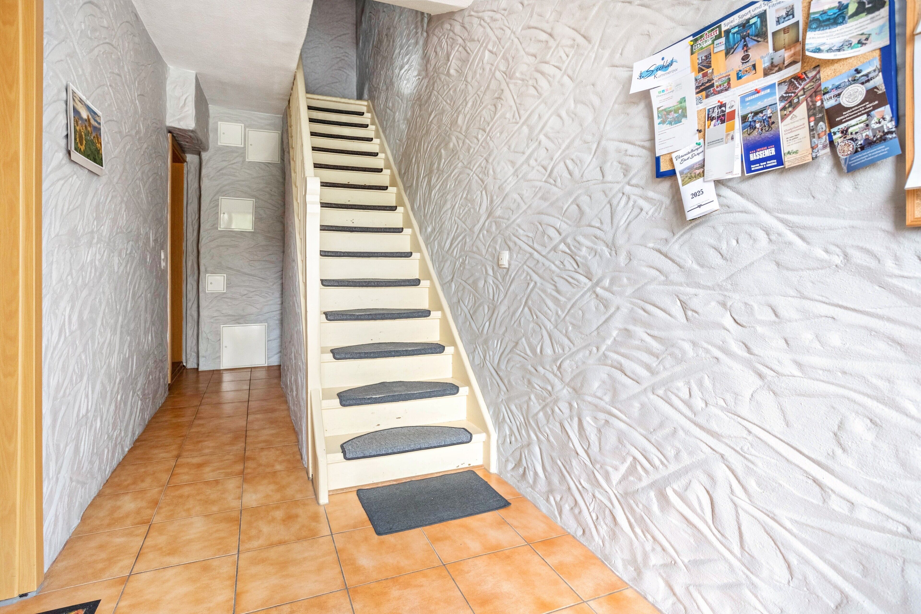 Eine Treppe mit Handlauf, einer Fußmatte und einem Bulletin Board mit verschiedenen Dokumenten.