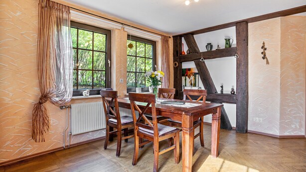 Un comedor con mesa y sillas de madera, ventanas amplias con cortinas y vistas al exterior.