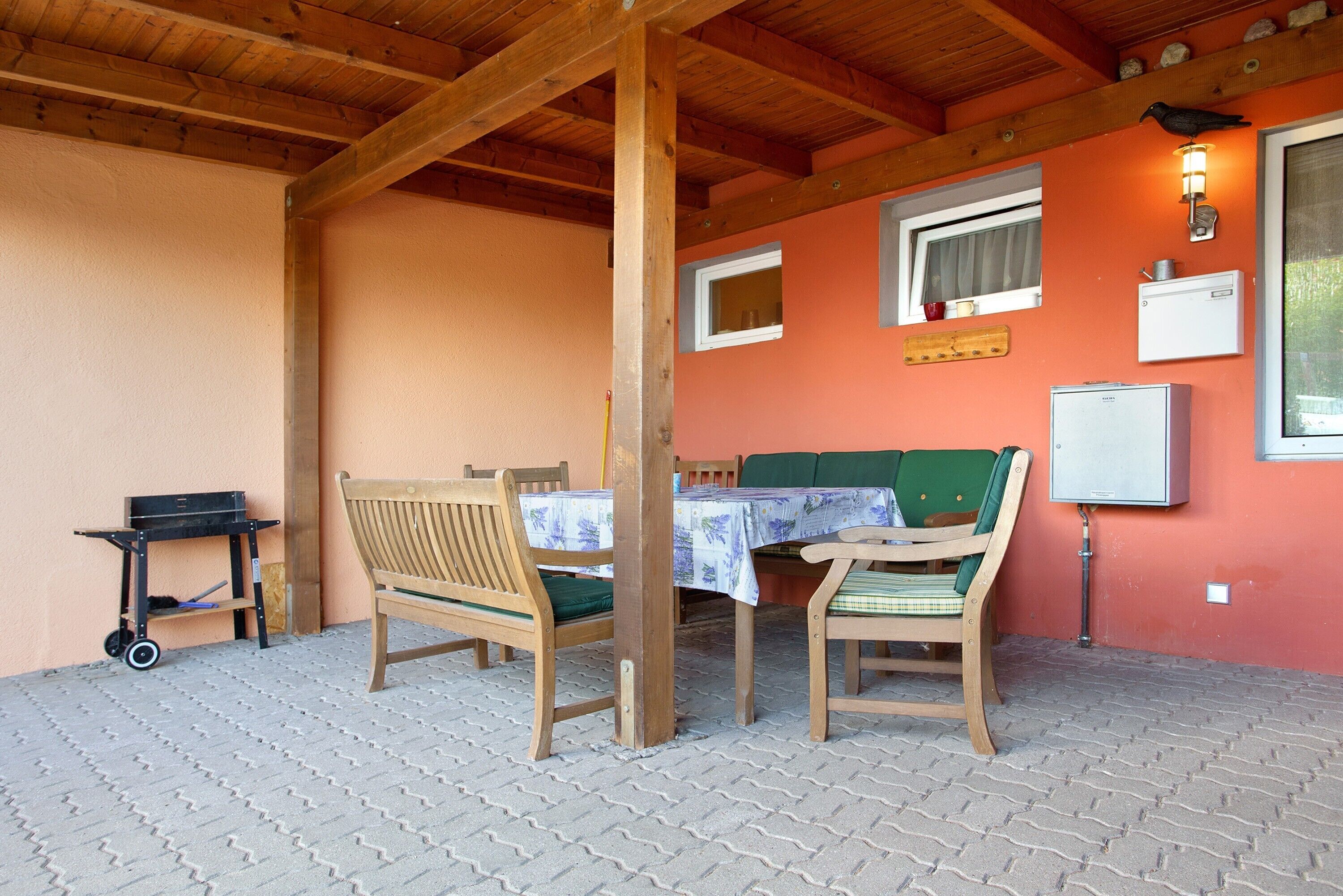 Un espacio de estar al aire libre cubierto con muebles de madera, una mesa y un carrito pequeño.