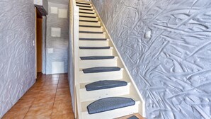Una escalera con una pared texturizada a un lado y una pared lisa al otro, que conduce a una puerta en la parte superior.