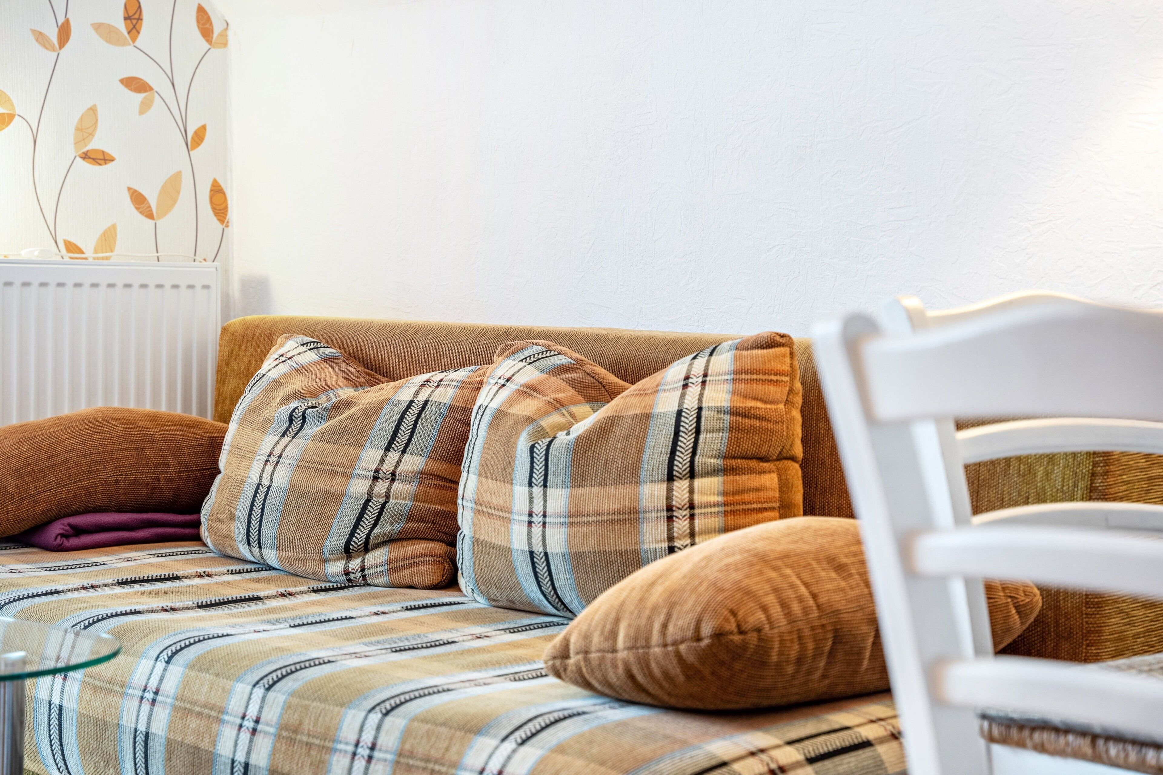Ein Sofa mit Karo-Kissen, ein weißer Sessel und eine Heizung.