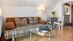 Una sala moderna con un sofá de cuadros, una mesa de centro de vidrio, una lámpara, una mesa de comedor con sillas y una zona de cocina al fondo.