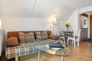 En moderne stue med en ternet sofa, et sofabord i glas, en lampe, et spisebord med stole, og et køkken i baggrunden.