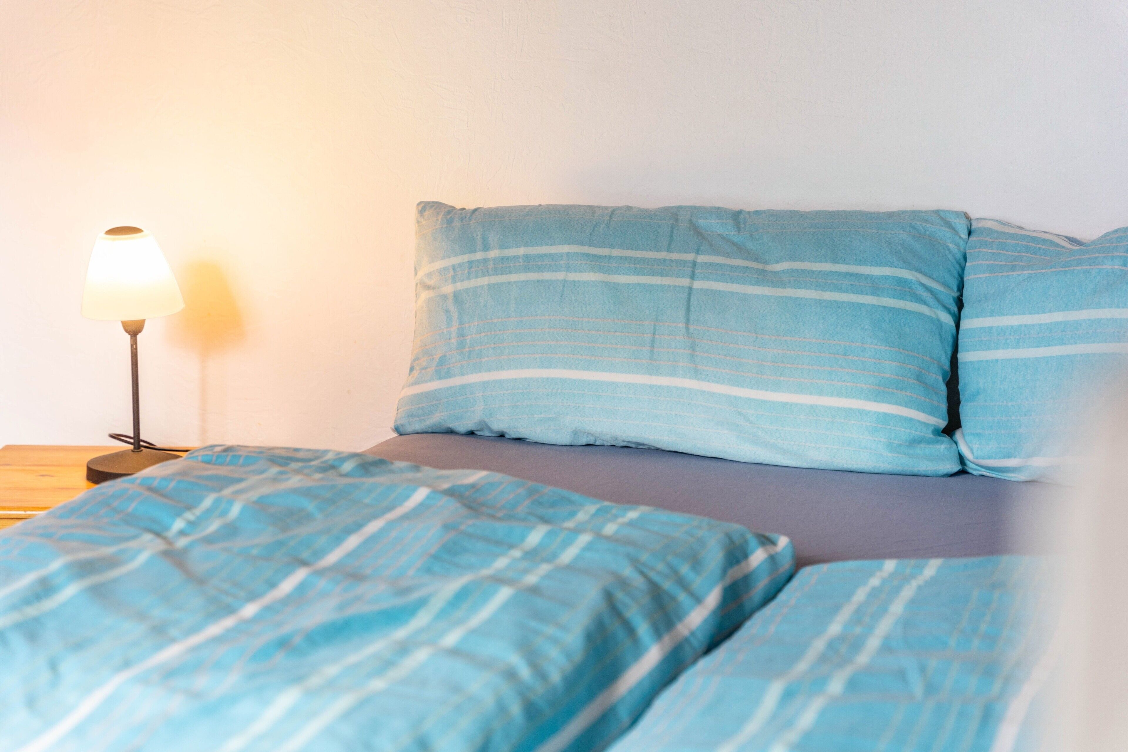 Ein Bett mit blau gestreifter Bettwäsche, eine Nachttischlampe und eine schlichte Wand.
