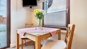 Een gezellig eetgedeelte met een houten tafel, een stoel, een vaas met bloemen en een aan de muur bevestigde televisie.