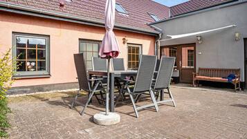 Eine Terrasse im Freien mit Tisch, Stühlen und einer Bank, sowie einem Sonnenschirm.