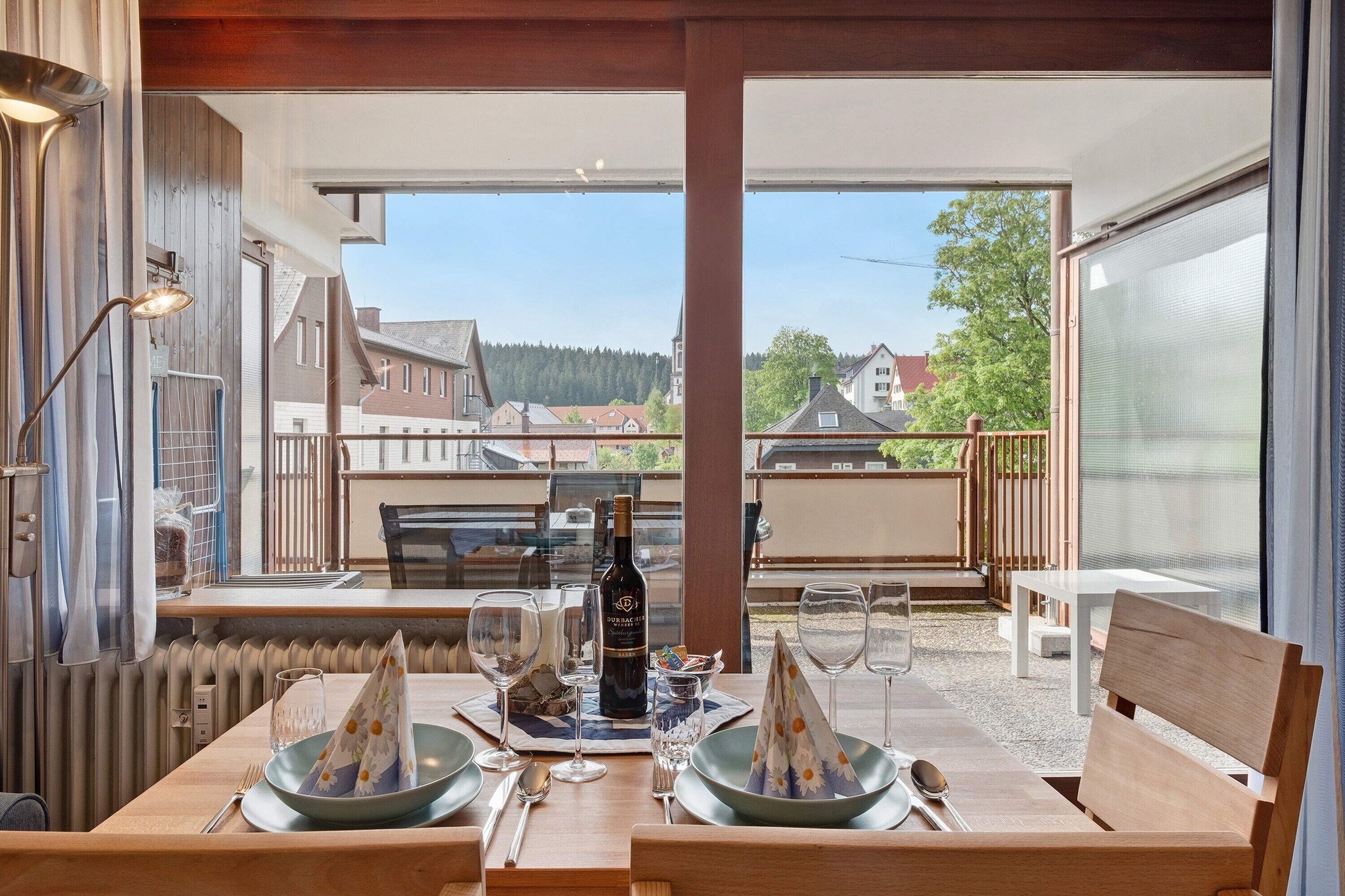 Un comedor con una mesa lista para dos personas, una botella de vino y vistas del barrio.