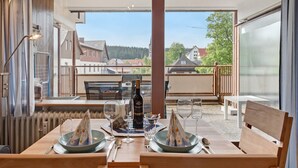 A dining area with a table set for two, a bottle of wine, and a view of the surrounding neighborhood. - Studio Apartment 'Schwarzwaldliebe' with Pool, Sauna, Mountain View, Balcony & Wi-Fi (Schönwald im Schwarzwald)