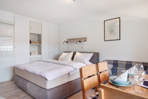 A bedroom with a bed, a dining table with chairs, a sofa, a wardrobe, and a framed picture on the wall.
