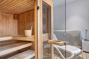 A sauna room with wooden benches, a glass door, a white radiator, and a white chair.