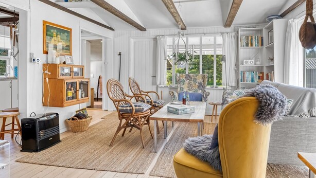 A spacious living room with a high ceiling, exposed wooden beams, a dining area with wicker chairs, a yellow armchair, and a bookshelf filled with books. - "Rieke" - 2km from the sea by Interhome (Blokhus)