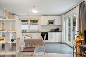 Una cocina moderna con muebles blancos, una mesa de comedor con sillas, un microondas integrado y un ventanal con cortinas.