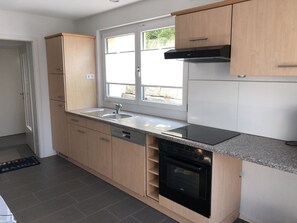 A modern kitchen with a dishwasher, oven, and a window providing natural light.