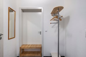 A room with a white door, a wooden coat rack, and a shelf unit.