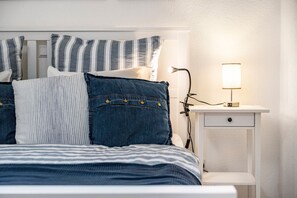 A bed with striped bedding, a bedside lamp, and a nightstand with a drawer.