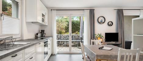Cozinha moderna com armários brancos, área de jantar com mesa e cadeiras, e porta de vidro deslizante para um jardim.