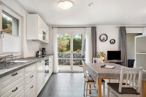 A modern kitchen with white cabinets, a dining area with a table and chairs, and a sliding glass door leading to a garden. - Apartment 'Bäumchenblick' with Terrace and Views of Greenery (Müllheim im Markgräflerland)