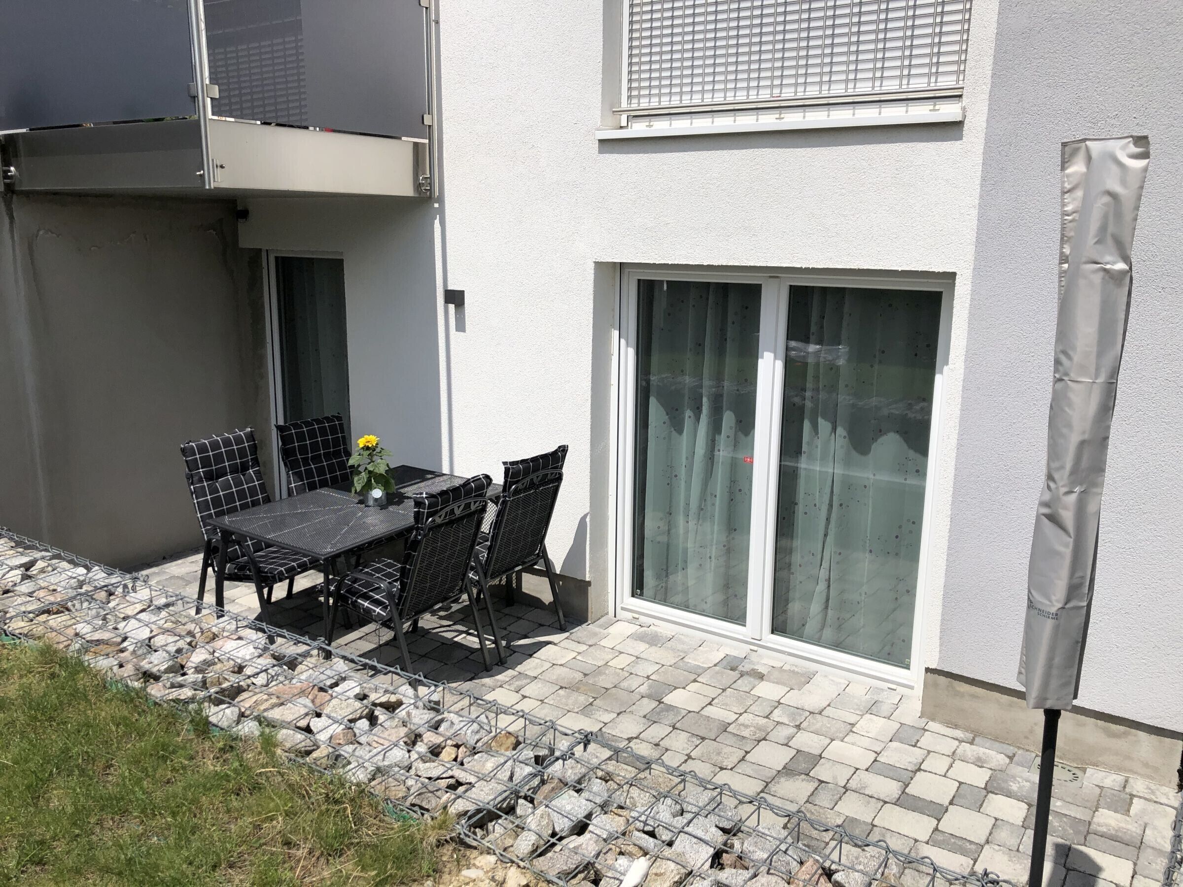 A patio with a table and chairs, a potted plant, and a building with a sliding glass door.