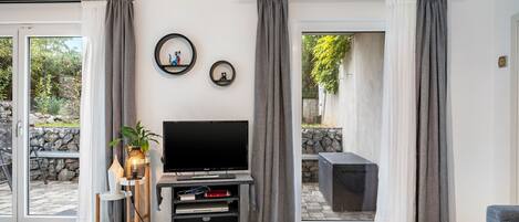 A living room with a flat-screen TV on a stand, a small table with a plant, and a seating area with a sofa.
