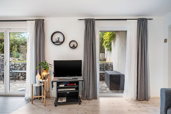 A living room with a flat-screen TV on a stand, a small table with a plant, and a seating area with a sofa.