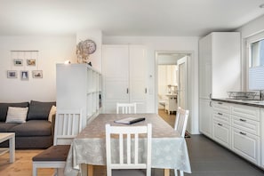 A modern, well-lit living space with a dining table, white furniture, and a kitchen area. - Apartment 'Bäumchenblick' with Terrace and Views of Greenery (Müllheim im Markgräflerland)