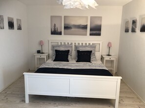 A white bed with striped bedding, two bedside tables with lamps, and three wall-mounted pictures.