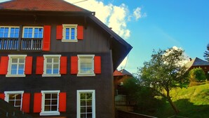 A multi-story building with a balcony, a wooden bench, and a staircase leading to a covered area. - Holiday Home 'Bernau' with Mountain View, Private Terrace and Wi-Fi (Bernau im Schwarzwald)