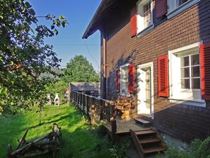 A brick house with red shutters, a wooden deck, and a small garden. - Holiday Home 'Bernau' with Mountain View, Private Terrace and Wi-Fi (Bernau im Schwarzwald)