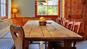 A wooden dining table with chairs, a fruit bowl, and a window with a view of greenery. - Holiday Home 'Bernau' with Mountain View, Private Terrace and Wi-Fi (Bernau im Schwarzwald)