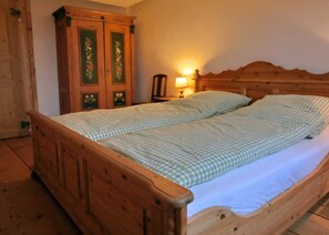 A wooden bed with a checkered bedspread and pillows, a nightstand with a lamp, and a wooden wardrobe with floral designs. - Holiday Home 'Bernau' with Mountain View, Private Terrace and Wi-Fi (Bernau im Schwarzwald)