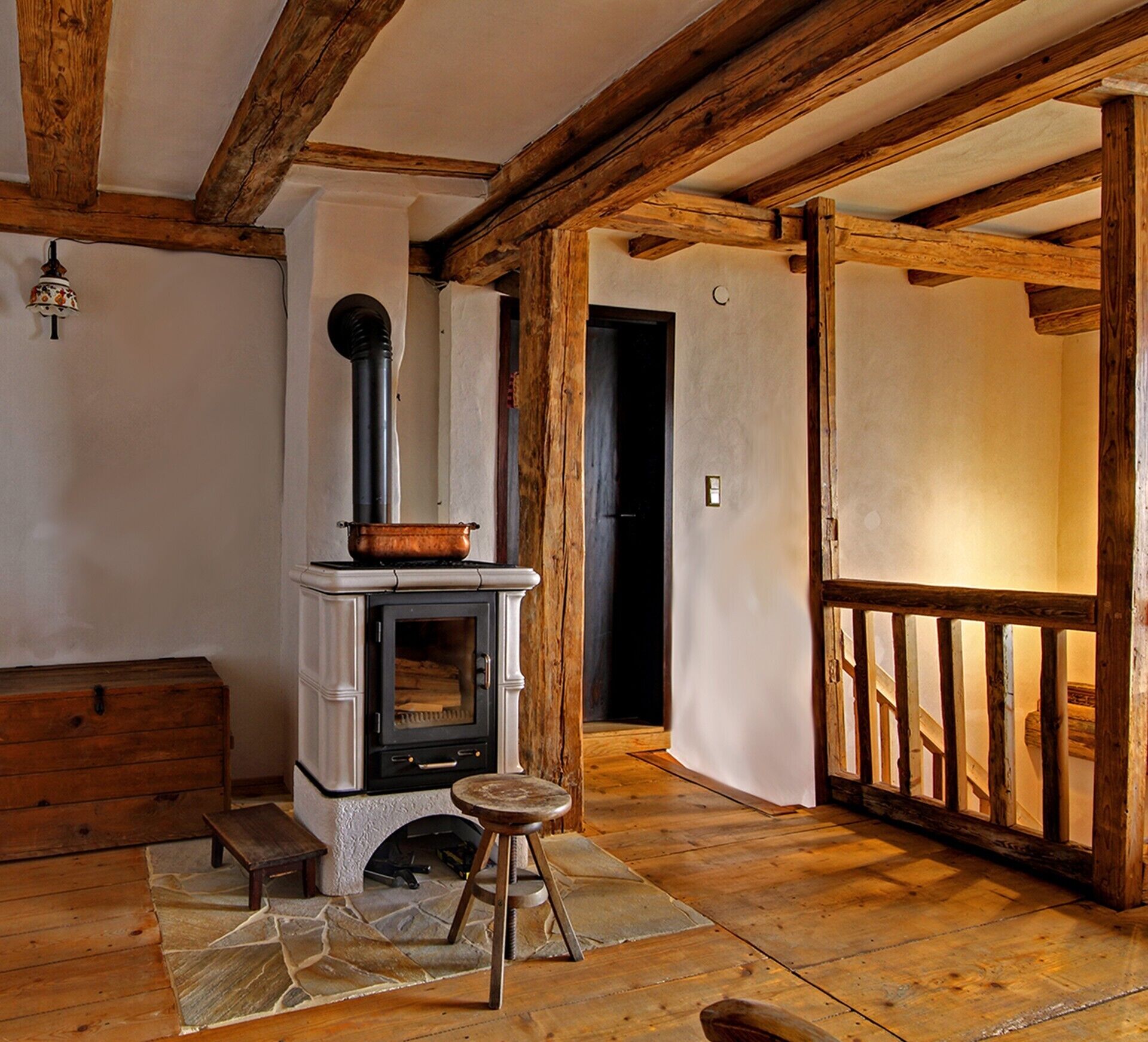 Une pièce rustique avec des poutres apparentes, une cheminée en pierre, un banc en bois et un petit tabouret.