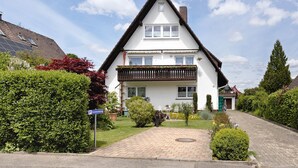 A two-story house with a sloped roof, a balcony, and a paved driveway.